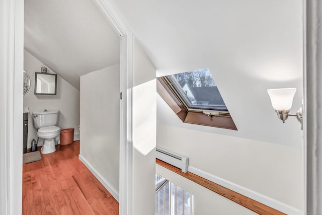 bathroom with lofted ceiling with skylight, toilet, wood-type flooring, and a baseboard heating unit