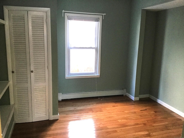 unfurnished bedroom featuring light hardwood / wood-style floors, a closet, and a baseboard heating unit