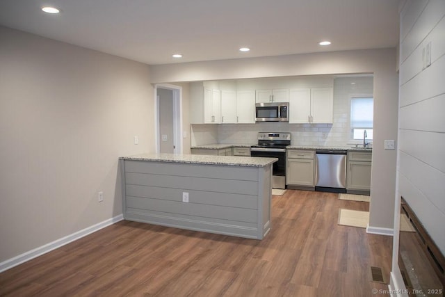 kitchen with tasteful backsplash, light stone counters, kitchen peninsula, wood-type flooring, and appliances with stainless steel finishes