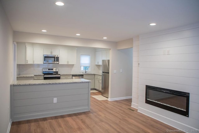 kitchen with white cabinetry, sink, stainless steel appliances, light stone counters, and kitchen peninsula