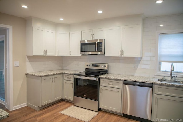 kitchen with light stone countertops, sink, stainless steel appliances, and light wood-type flooring