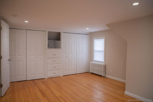 unfurnished bedroom featuring light hardwood / wood-style floors, radiator, and two closets