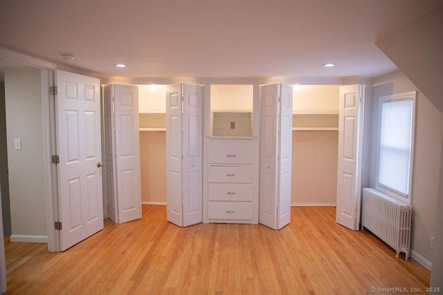 unfurnished bedroom with a spacious closet, radiator heating unit, and light hardwood / wood-style flooring