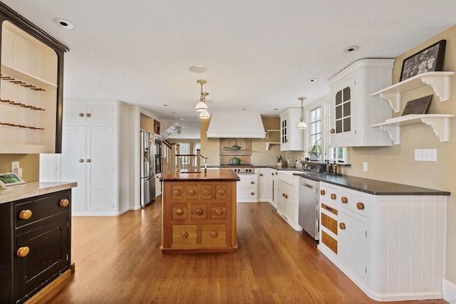 kitchen with appliances with stainless steel finishes, a kitchen island, white cabinets, and decorative light fixtures