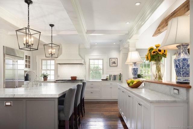 kitchen featuring stainless steel appliances, backsplash, custom exhaust hood, beam ceiling, and a center island with sink