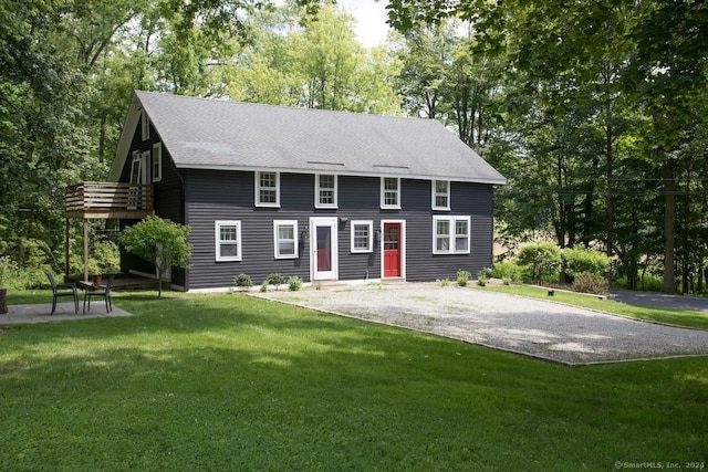 colonial inspired home featuring driveway, roof with shingles, a front yard, and a balcony