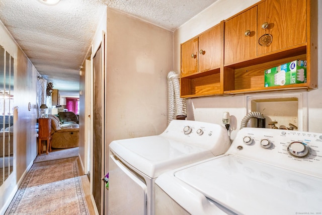 washroom featuring washing machine and clothes dryer, cabinet space, and a textured ceiling