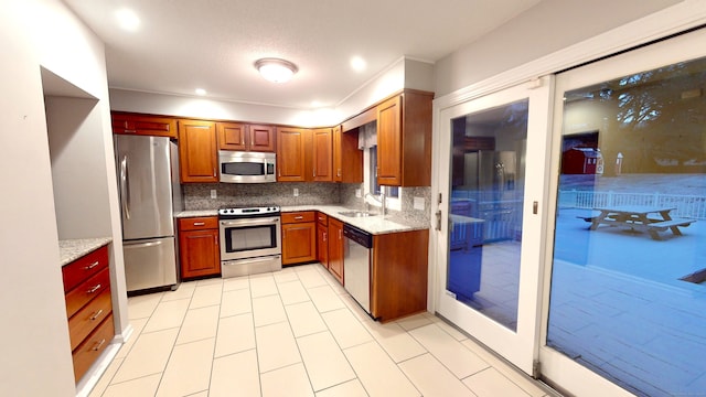 kitchen with decorative backsplash, sink, light stone counters, and appliances with stainless steel finishes