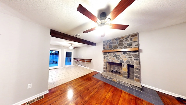 unfurnished living room with ceiling fan, beamed ceiling, a textured ceiling, a fireplace, and hardwood / wood-style flooring