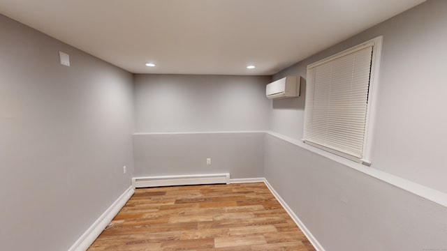 basement featuring a wall mounted air conditioner, light wood-type flooring, and a baseboard heating unit