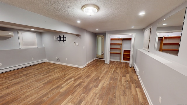 basement with a wall mounted AC, light hardwood / wood-style flooring, a baseboard radiator, and a textured ceiling