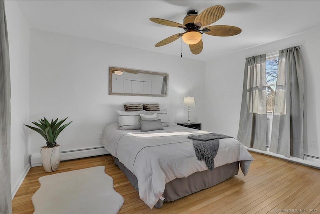 bedroom with a baseboard heating unit, ceiling fan, and wood-type flooring