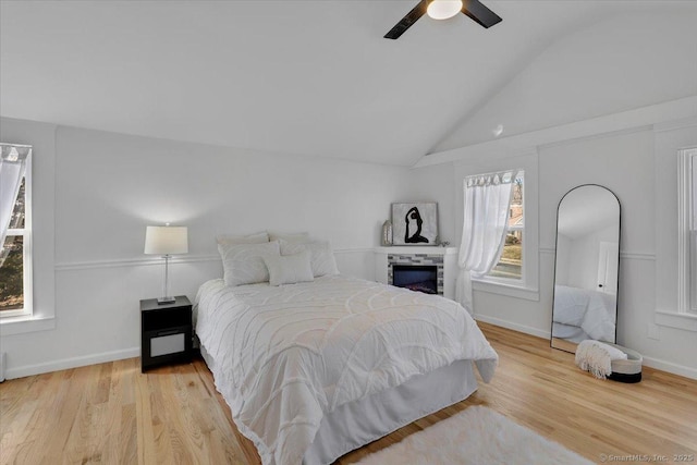 bedroom with ceiling fan, light hardwood / wood-style floors, vaulted ceiling, and multiple windows