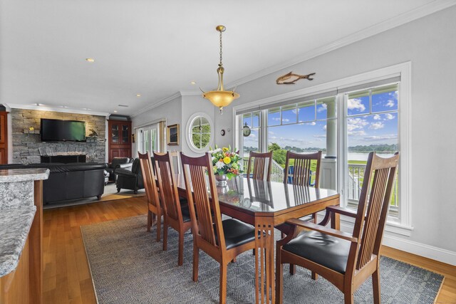 dining room featuring light hardwood / wood-style flooring, a stone fireplace, and crown molding