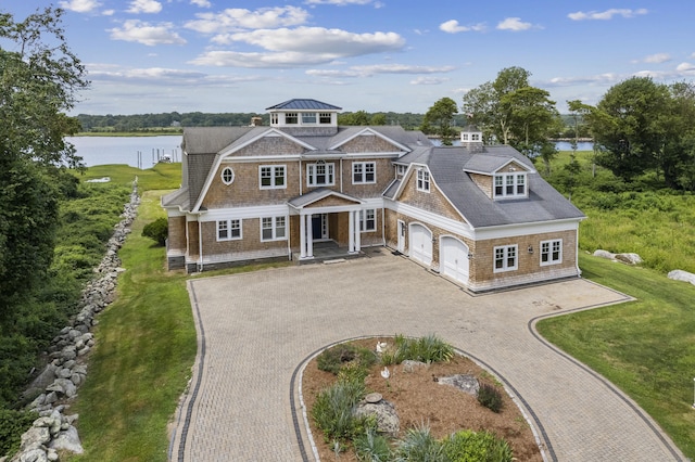 shingle-style home with driveway, a water view, a garage, and a front yard