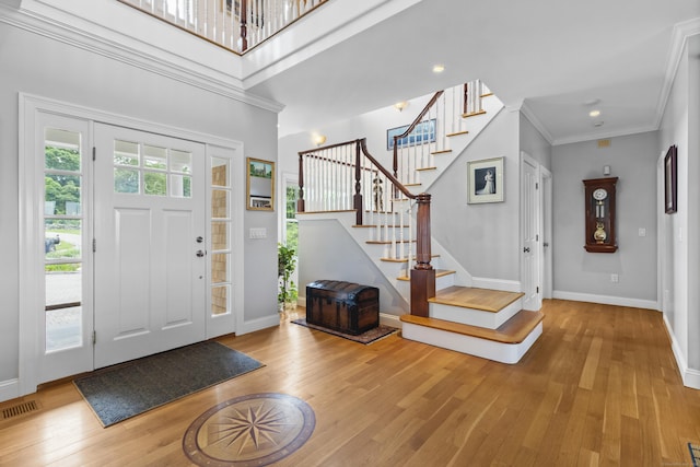 foyer entrance with a towering ceiling, light hardwood / wood-style floors, and crown molding