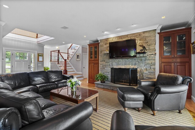 living area with stairs, a stone fireplace, light wood finished floors, and ornamental molding