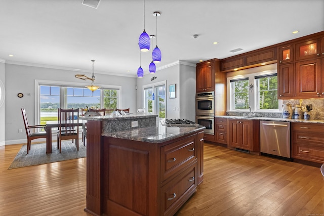 kitchen featuring a center island, crown molding, appliances with stainless steel finishes, decorative light fixtures, and light hardwood / wood-style floors