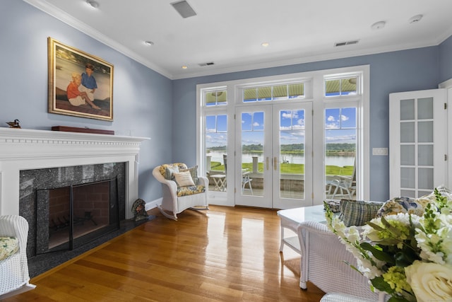 living room featuring french doors, a premium fireplace, light hardwood / wood-style floors, a water view, and ornamental molding