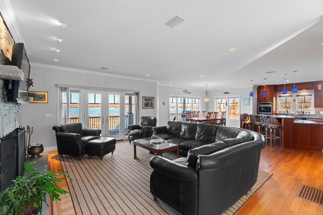 living room featuring visible vents, ornamental molding, a stone fireplace, french doors, and light wood-style floors