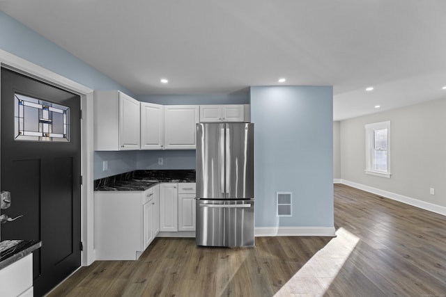 kitchen with white cabinets, dark hardwood / wood-style flooring, stainless steel refrigerator, and dark stone counters