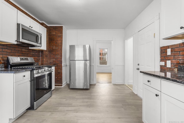 kitchen featuring dark stone countertops, white cabinets, stainless steel appliances, and light wood-type flooring