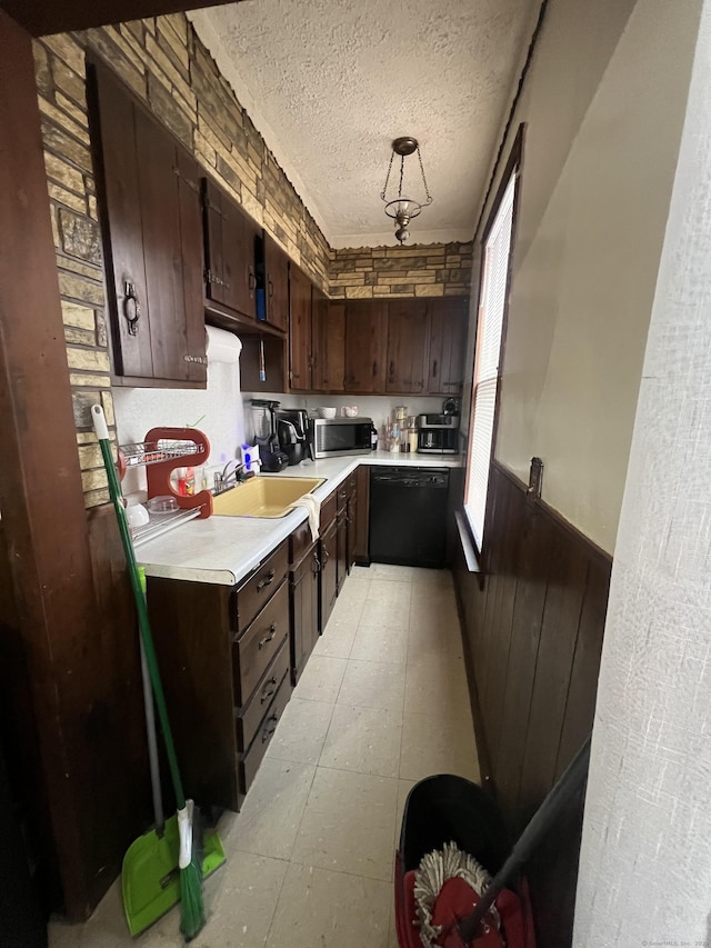 kitchen featuring a textured ceiling, wooden walls, sink, pendant lighting, and dishwasher