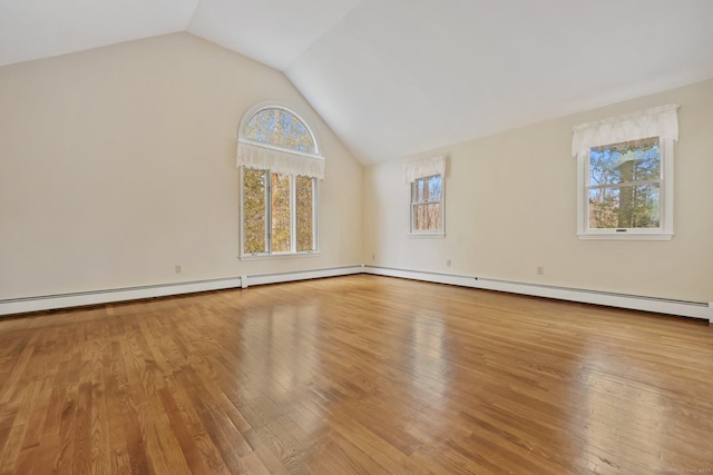 empty room featuring baseboard heating, a healthy amount of sunlight, vaulted ceiling, and light hardwood / wood-style flooring