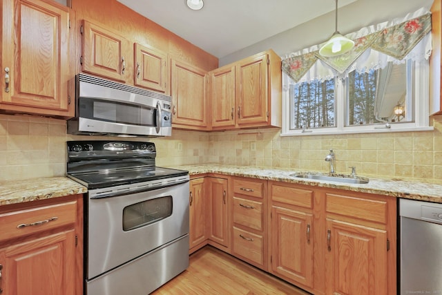 kitchen with light stone counters, stainless steel appliances, decorative light fixtures, and sink