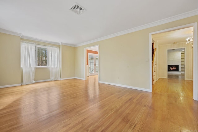 empty room featuring an inviting chandelier, ornamental molding, a fireplace, and light hardwood / wood-style floors