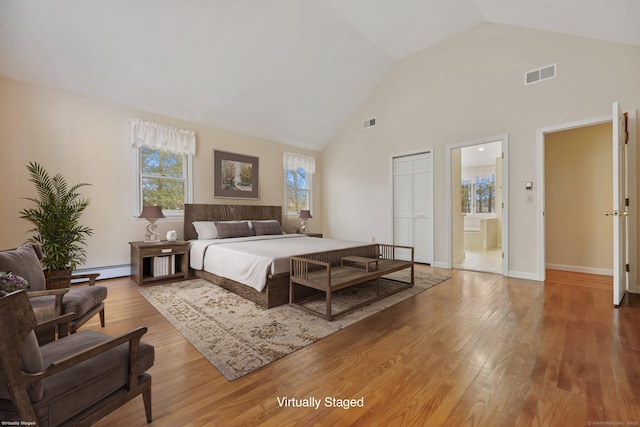 bedroom with lofted ceiling, light hardwood / wood-style flooring, a baseboard heating unit, ensuite bathroom, and a closet