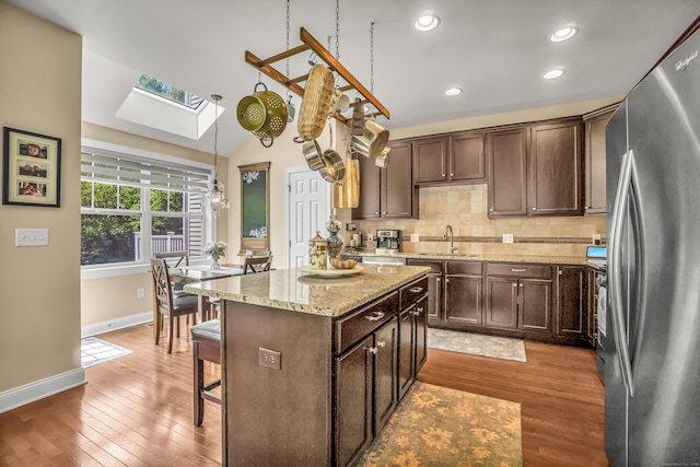 kitchen with decorative backsplash, lofted ceiling with skylight, a kitchen island, sink, and stainless steel refrigerator