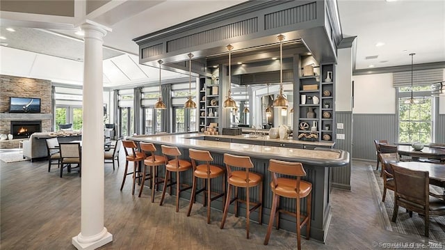 bar with decorative columns, a stone fireplace, pendant lighting, and dark wood-type flooring