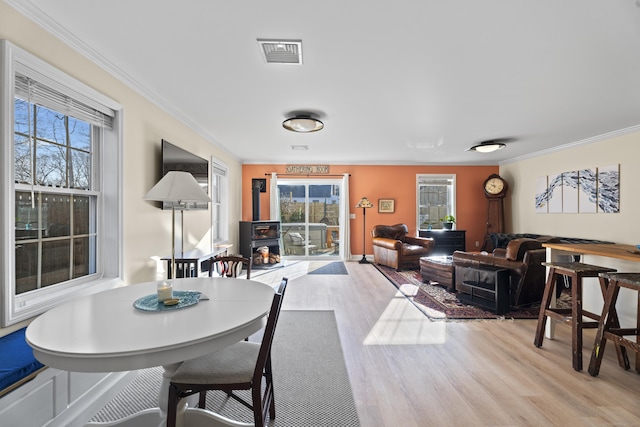 dining room with a wood stove, a wealth of natural light, crown molding, and light wood-type flooring