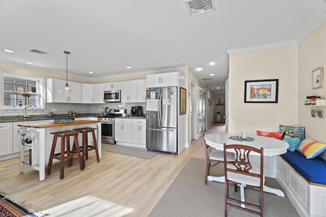 kitchen with white cabinetry, sink, hanging light fixtures, stainless steel appliances, and a breakfast bar