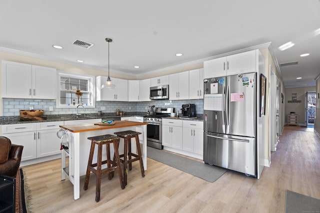 kitchen featuring white cabinets, decorative light fixtures, stainless steel appliances, and butcher block countertops