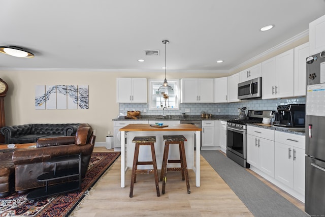 kitchen featuring appliances with stainless steel finishes, sink, light hardwood / wood-style flooring, white cabinetry, and hanging light fixtures