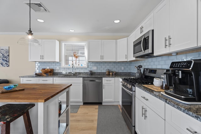 kitchen with decorative backsplash, stainless steel appliances, white cabinets, light hardwood / wood-style floors, and hanging light fixtures