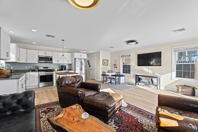 living room featuring crown molding, sink, and light wood-type flooring