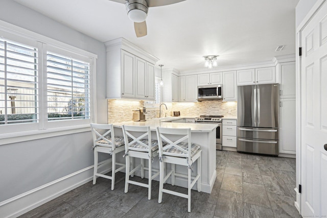 kitchen with kitchen peninsula, hanging light fixtures, a kitchen bar, white cabinetry, and stainless steel appliances