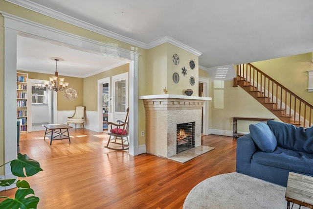 living room featuring a fireplace, wood-type flooring, ornamental molding, and a notable chandelier