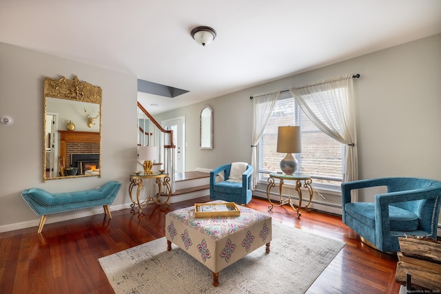 living area featuring hardwood / wood-style floors, a baseboard radiator, and a brick fireplace