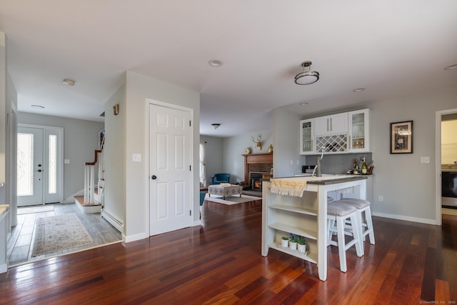 kitchen featuring a brick fireplace, a baseboard radiator, white cabinetry, and dark wood-type flooring