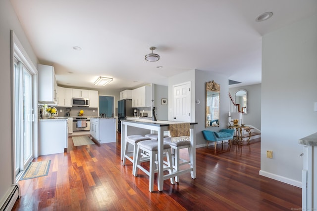 kitchen with baseboard heating, white cabinets, dark hardwood / wood-style floors, a kitchen island, and appliances with stainless steel finishes