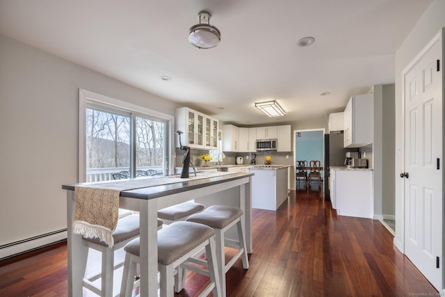 kitchen featuring dark wood-type flooring, white cabinets, a baseboard radiator, a kitchen island, and stainless steel appliances