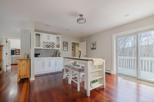 kitchen with dark hardwood / wood-style floors, white cabinetry, an island with sink, and a baseboard heating unit