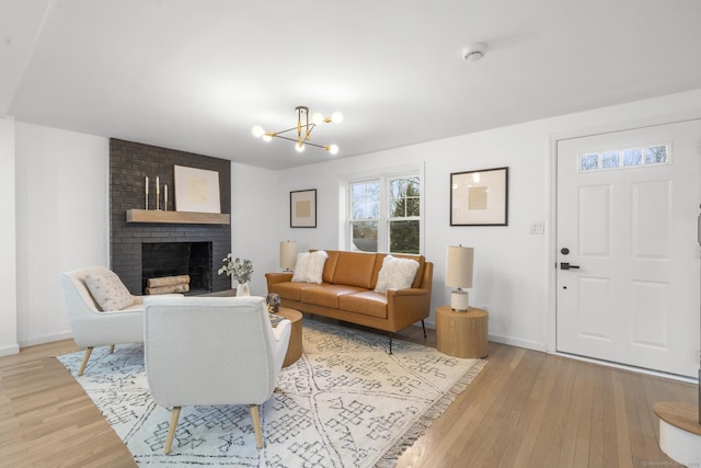 living room with an inviting chandelier, light hardwood / wood-style floors, and a brick fireplace