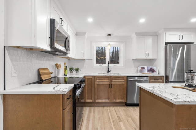 kitchen with sink, hanging light fixtures, light hardwood / wood-style floors, white cabinets, and appliances with stainless steel finishes