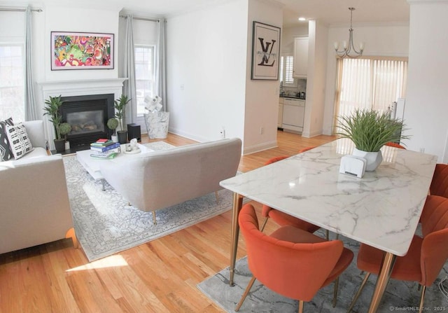 living room featuring a notable chandelier, light hardwood / wood-style floors, a healthy amount of sunlight, and ornamental molding