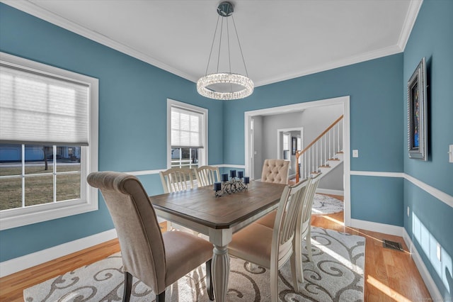 dining area with a notable chandelier, light wood-type flooring, and ornamental molding